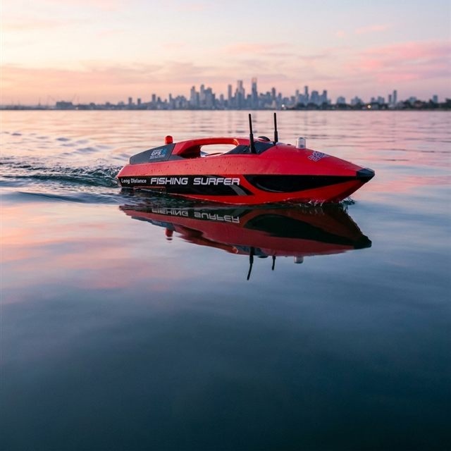 Red Joysway Fishing Surfer RC bait boat running across calm water at sunset