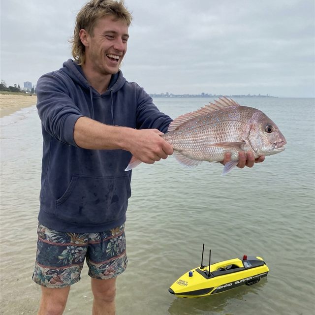 Angler laughing as he holds up a pink snapper on a beach